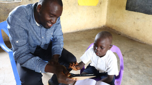 A teacher in Kenya holds an iPad while a young student taps the screen.