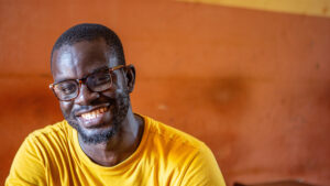 Iliezer smiles at the camera. He's wearing a bright yellow t-shirt.