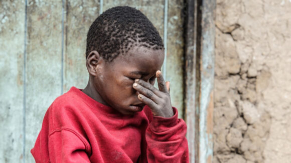 Mwiza sits on a step and rubs his eyes.