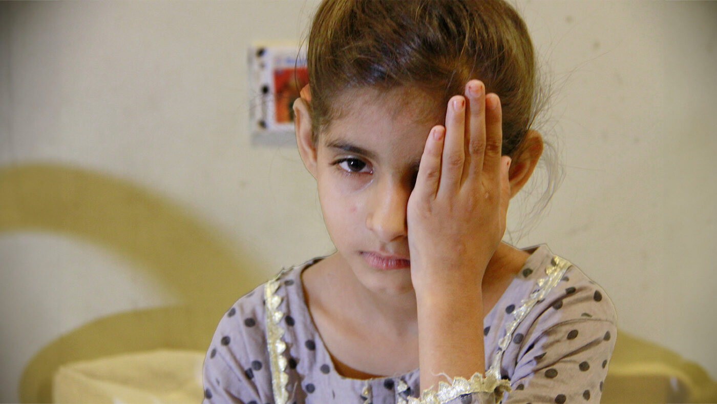 Nine-year-old Nayab covers her eye with her hand.