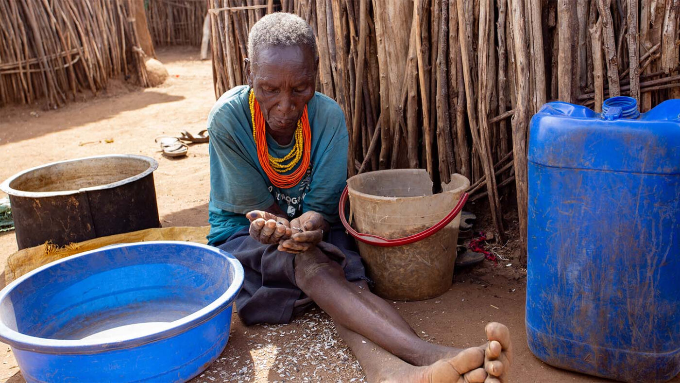 Nyangan looking at grains in her hands whilst sitting on the floor surrounded by containers