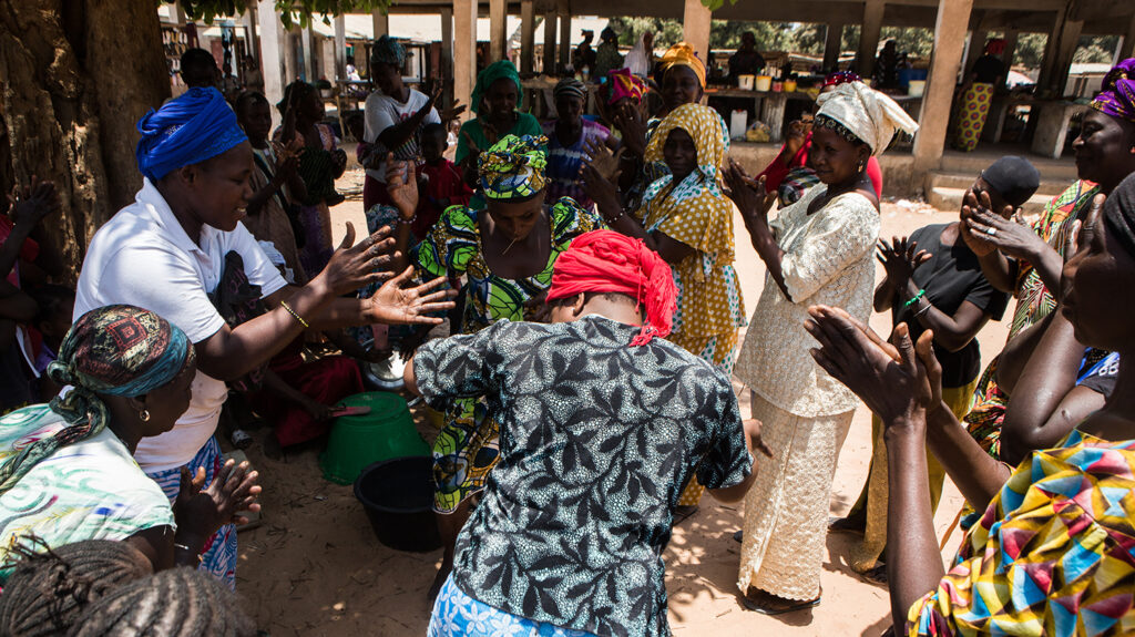 A large group of women dance and clap while celebrating the elimination of trachoma in The Gambia.