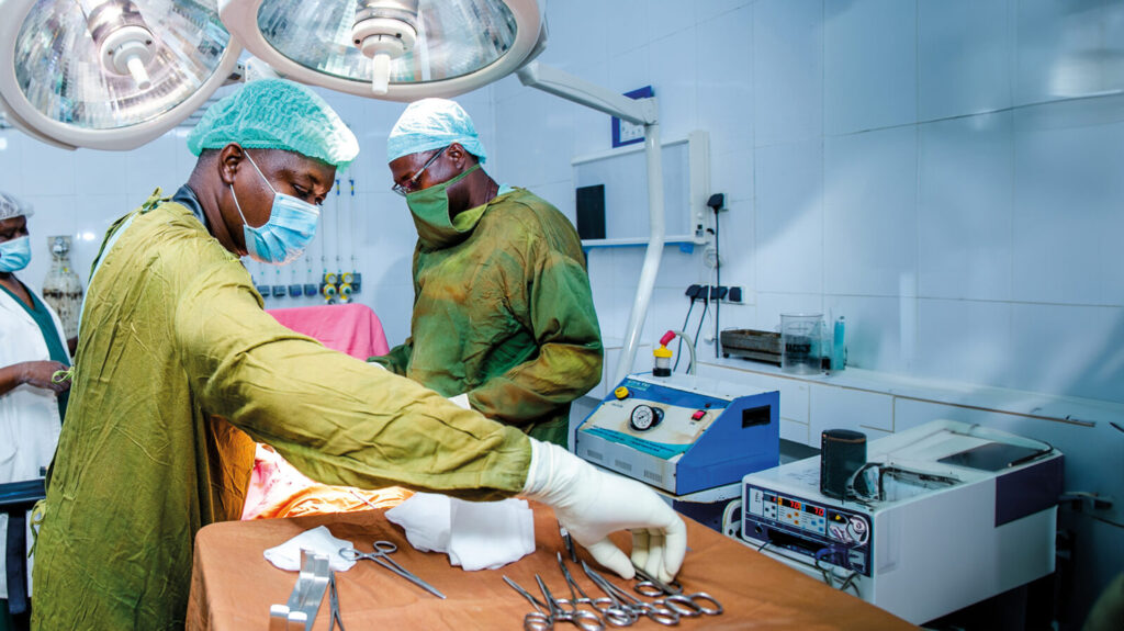 Two doctors in surgical scrubs prepare equipment inside an operating theatre.