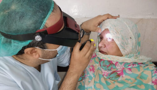 A male eye health worker in Pakistan uses a torch to check a woman's eyes for signs of advanced trachoma.