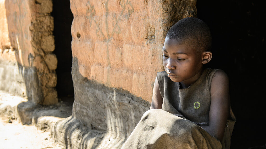 Mary looks sad sitting outside her home. She's crossing her arms in front of her looking tense. Her eyes are downcast.