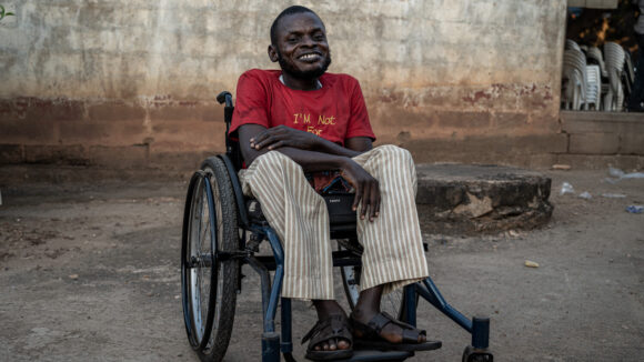 A man in a wheelchair smiles outside a brick building.