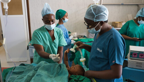 In an operating theatre, a surgeon and a nurse prepare baby Ebenezeri for her cataract operation. The medical staff are wearing green scrubs and surgical masks.