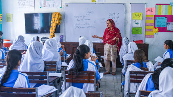 Schoolchildren watch their teacher point to a classroom whiteboard.