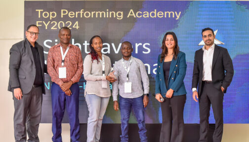 Sightsavers’ programme officer Salome Njeri Mbugua-Mutua receives the award on stage alongside two academy instructors.