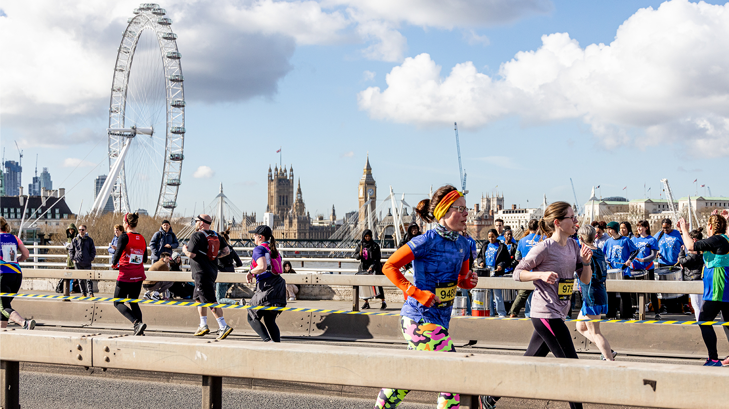Runners cross a bridge with the London Eye and Big Ben in the background.