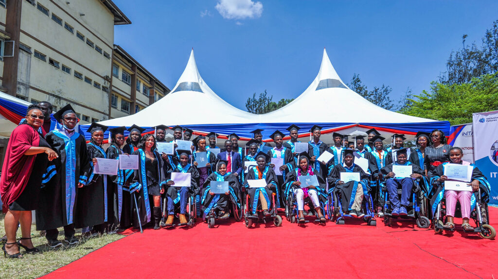 Graduates from the IT Bridge Academy pose for a group photo. They're wearing graduation robes and hats. Students using wheelchairs are seated in the front row.