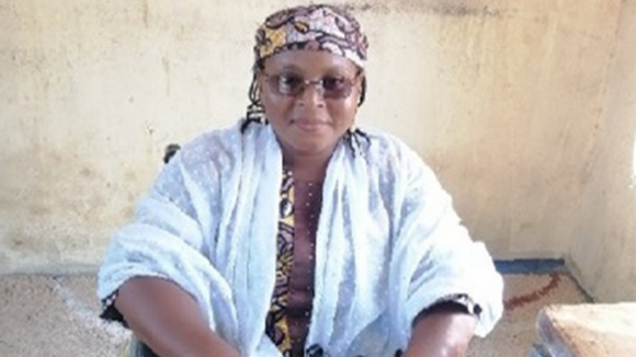 Bilkisu wears sunglasses and a bandana while smiling for a photograph.