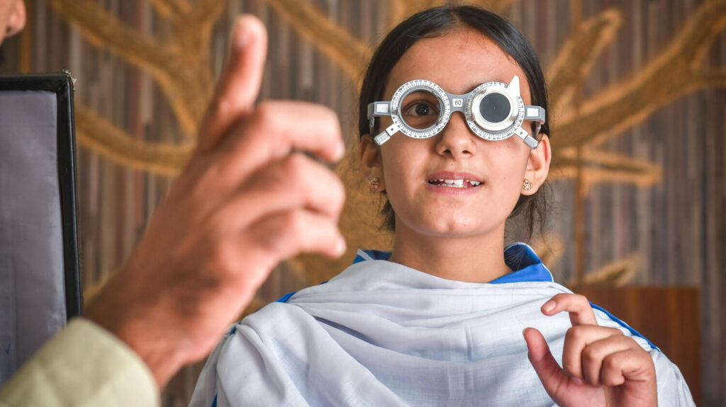 A female student wears eye test glasses during a refractive error examination.
