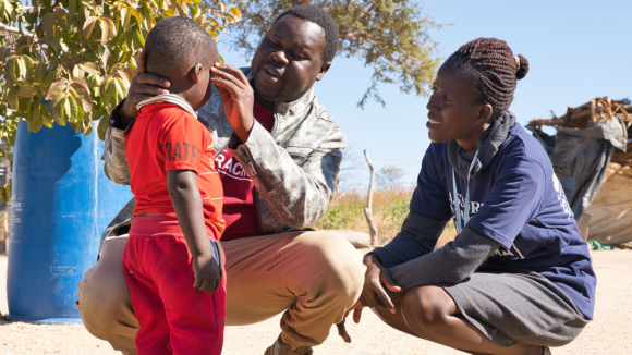 A woman and a man check the vision of a young child outside.