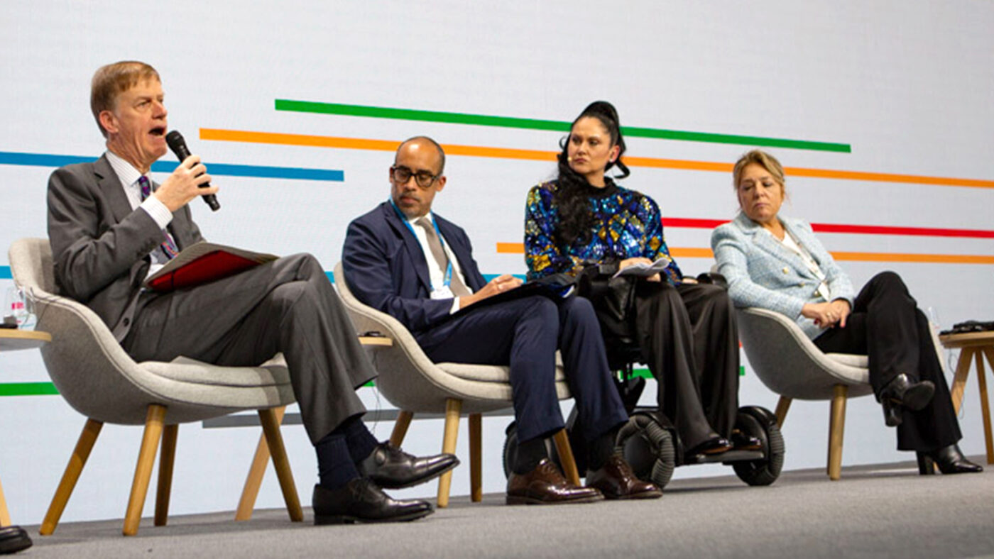 A panel of two men and two women sit on stage at the summit. One of the men is holding a microphone.