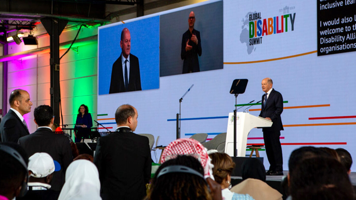 The main stage at the summit, with a large audience watching Olaf Scholz on stage.