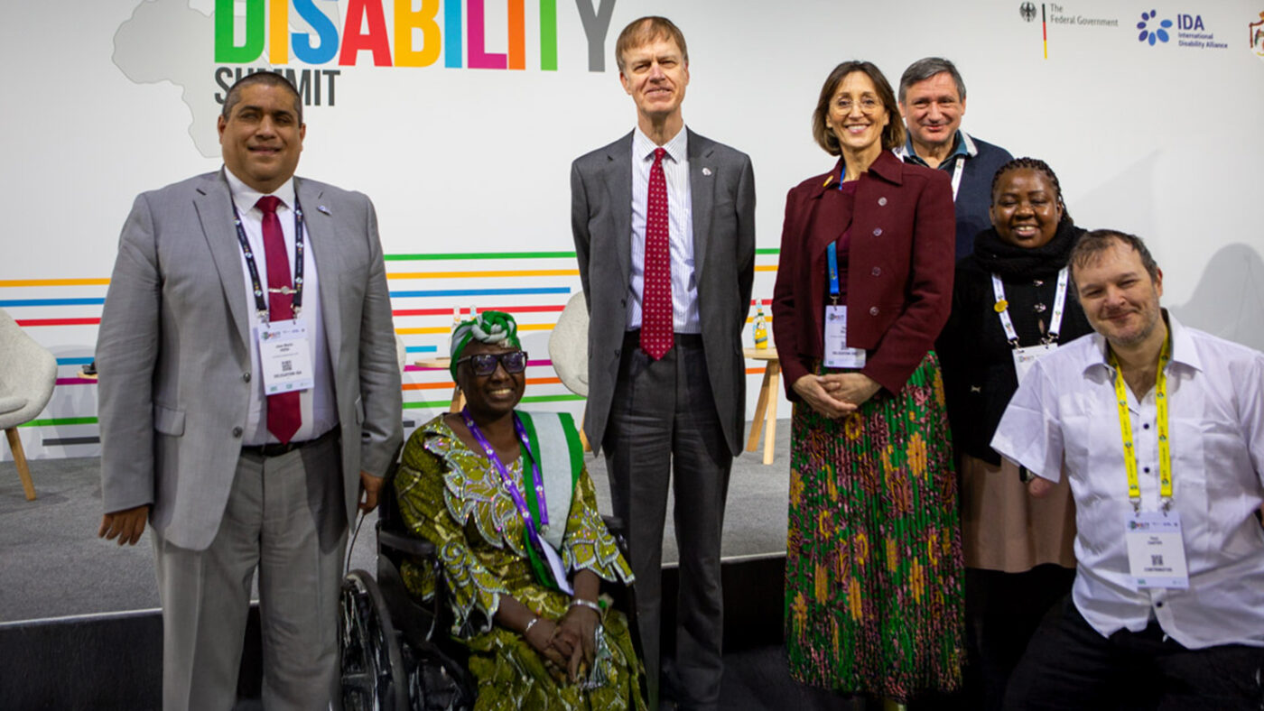 A group of seven smartly dressed people, some with disabilities, gather for a photo at the summit