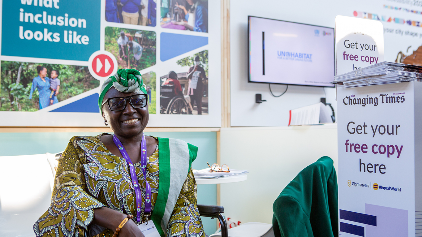 Lois smiles while sitting in a wheelchair beside The Changing Times newspaper stand.