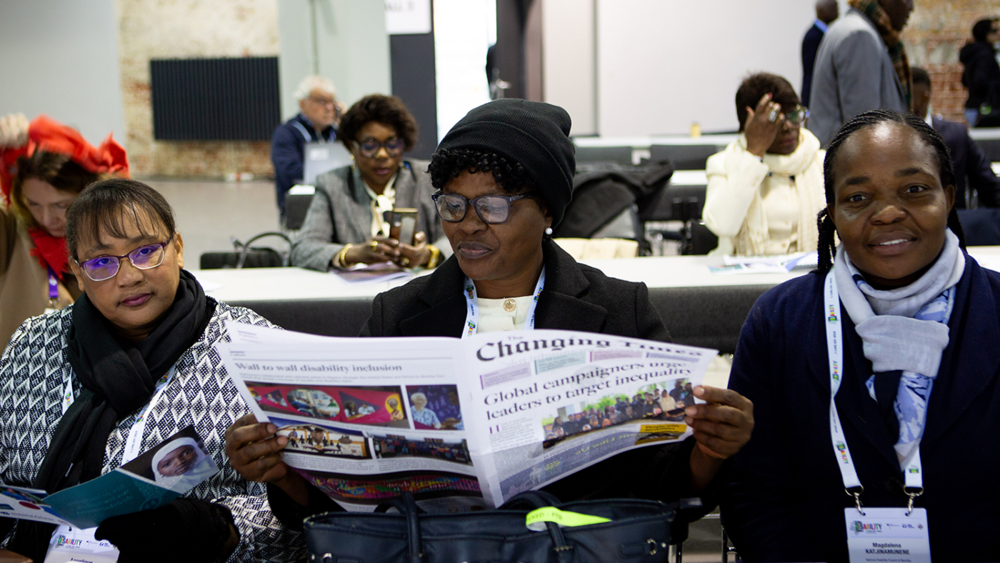 Three women sit at a desk with one woman reading Sightsavers' The Changing Times newspaper.
