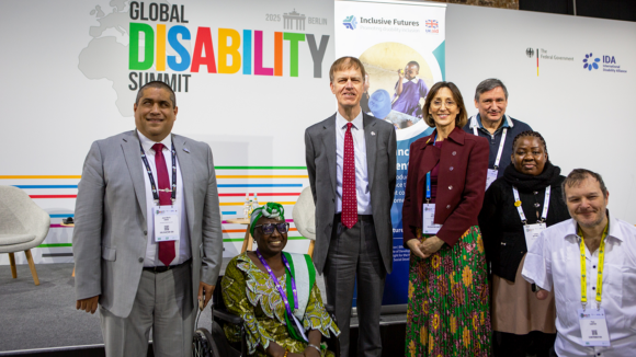 Seven people pose in front of the Global Disability Summit logo. One person is in a wheelchair and another has a physical disability.