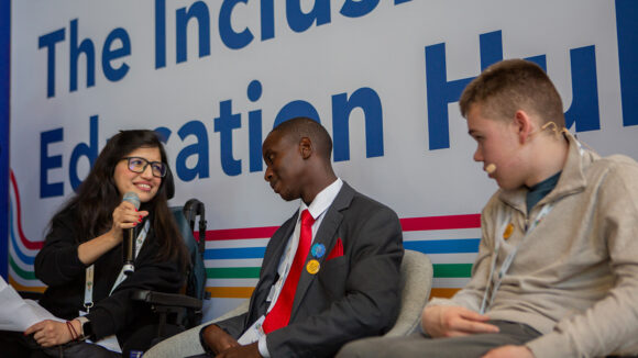Abia holds a microphone while speaking with Tapiwa and James during a panel session at the Global Disability Summit.