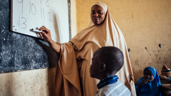 Muhammad looks at the whiteboard in his classroom as his teacher points to the board.