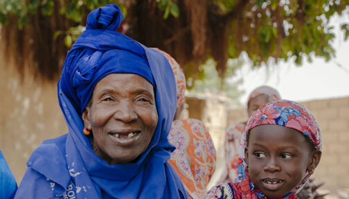 Nar, who had successful treatment for trachoma, sits outside with her two grandchildren. They are all smiling.