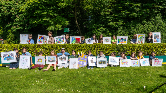 Two rows of children pose outside with their artworks.