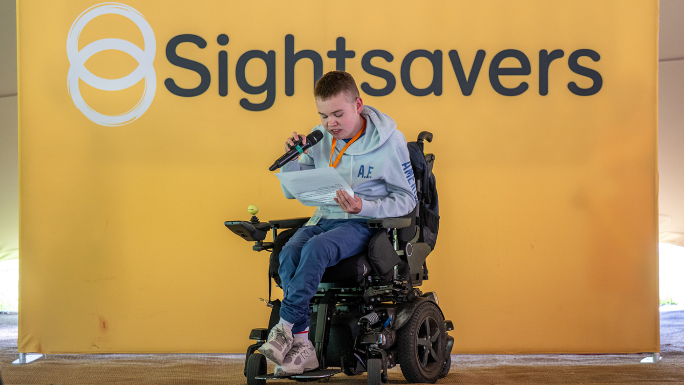 James Casserly, who uses a wheelchair, holds a microphone while reading from a sheet of paper.