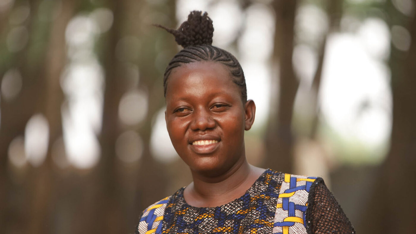 Magdalene, who is blind, stands outside with trees behind her.