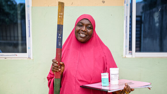 Amina holds a dose pole, paperwork and medication.