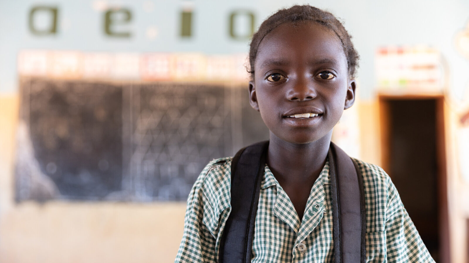 Ruth, a 10 year old student from Zambia, stands inside a classroom in her school.