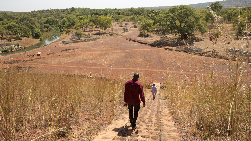Two men walk through dusty fields.