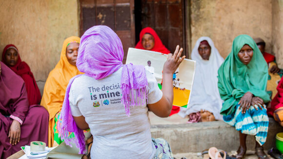 A female workshop facilitator shows a group of women a booklet about family planning.