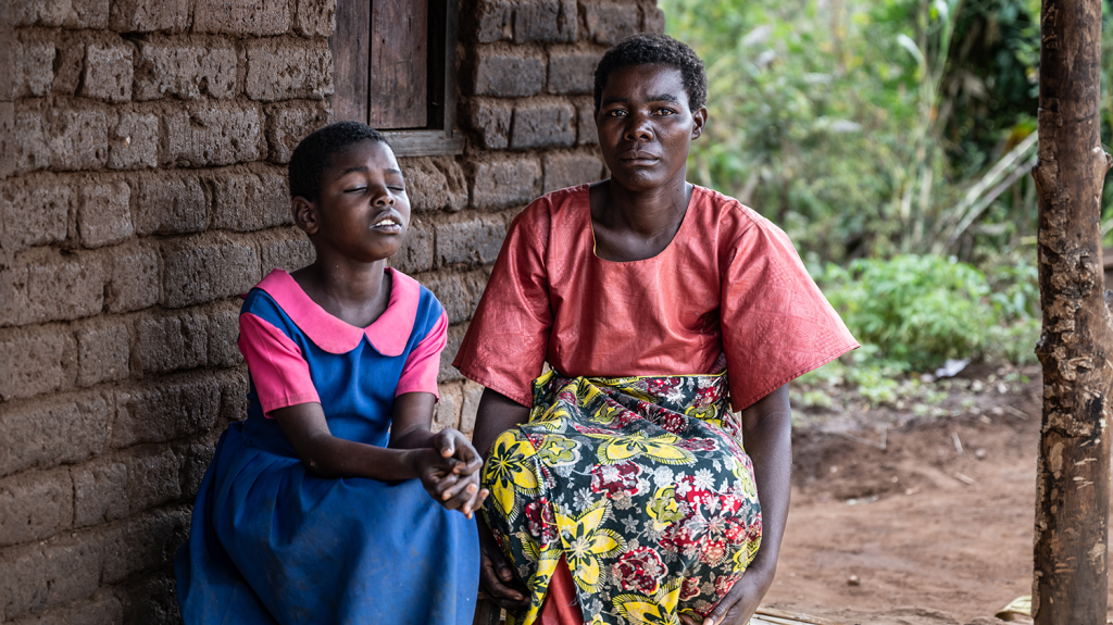 Melia, a young girl, sat outside her home in Malawi with her mother, Veronica.