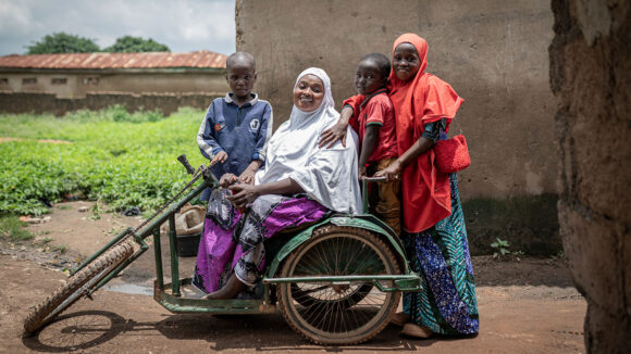 A woman sits on an accessibility scooter surrounded by three children.