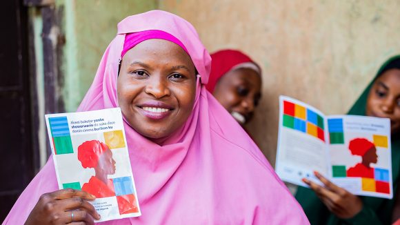 A woman wearing a pink chador holds up a booklet about inclusive family planning.