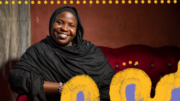 A woman wearing a black chador smiles while sitting on a sofa.