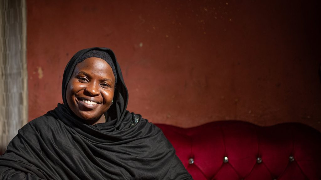 A woman wearing a black chador smiles while sitting on a sofa.