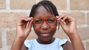 Ivania, a 14-year-old girl from Mozambique, holds her new red glasses in front of her eyes.