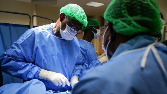 A male surgeon wearing medical scrubs performs surgery.