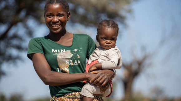 Lupula holds her daughter Sarah on her hip and smiles at the camera.