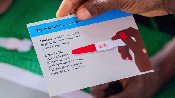 A hand holding a card with a drawing of a pregnancy test.