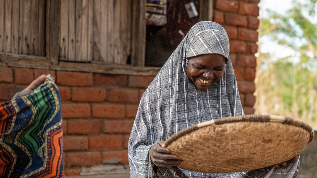 Ruth smiles while sorting millet using a wicker basket.