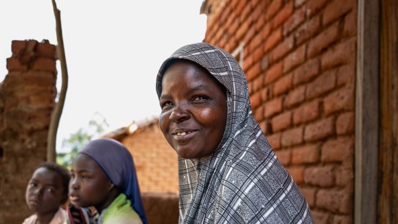 Ruth, who is wearing a head scarf, sits in front of a brick wall. Two of her children are sitting next to her.