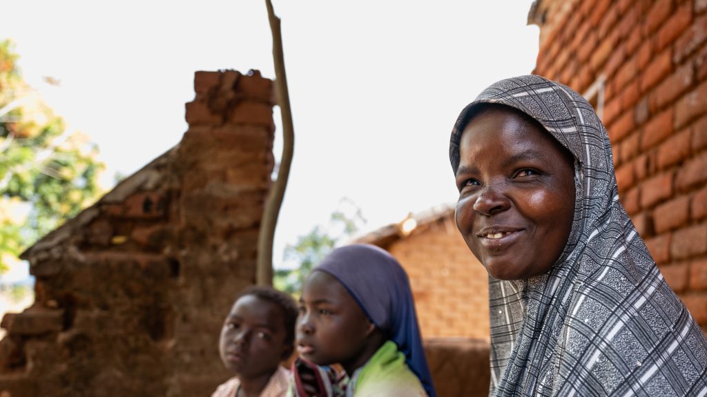 Ruth, who is wearing a head scarf, sits in front of a brick wall. Two of her children are sitting next to her.