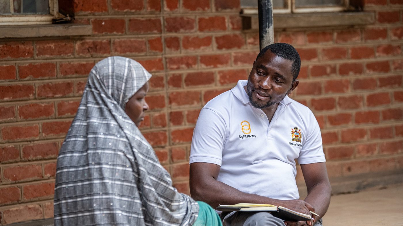 Ruth sits outside with Benjamin, who is wearing a white polo shirt with the Sightsavers logo.