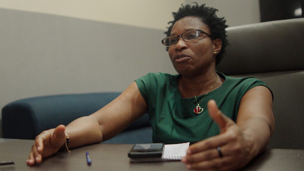A woman sits at a desk talking to another person.