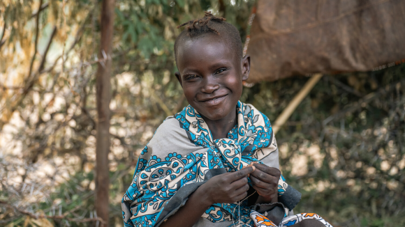 Namoite is sat outside smiling whilst making ornamental beads in Kenya.