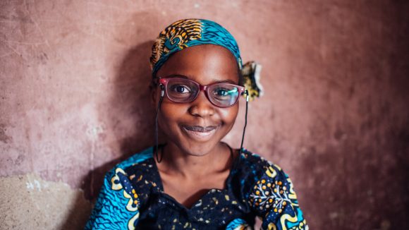 A girl wearing a colourful headwrap and a pair of glasses.